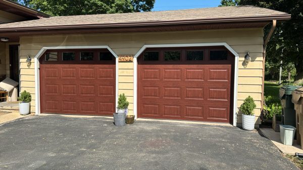 Two brown residential garage doors installed on a detached garage with beige siding and decorative planters.
