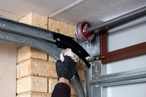 How To Lubricate Garage Doors? 1 person wipes off garage door tracks